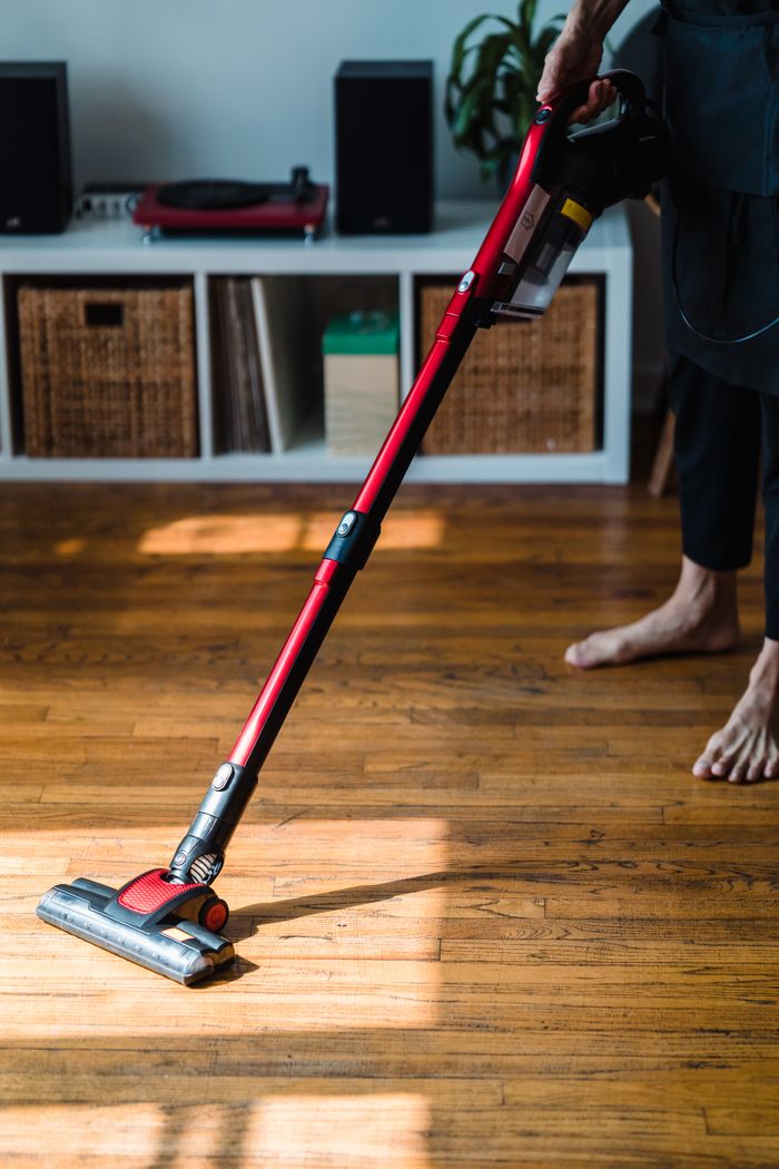 home-services-02 Person vacuuming a wooden floor with a modern appliance, highlighting efficient home cleaning.