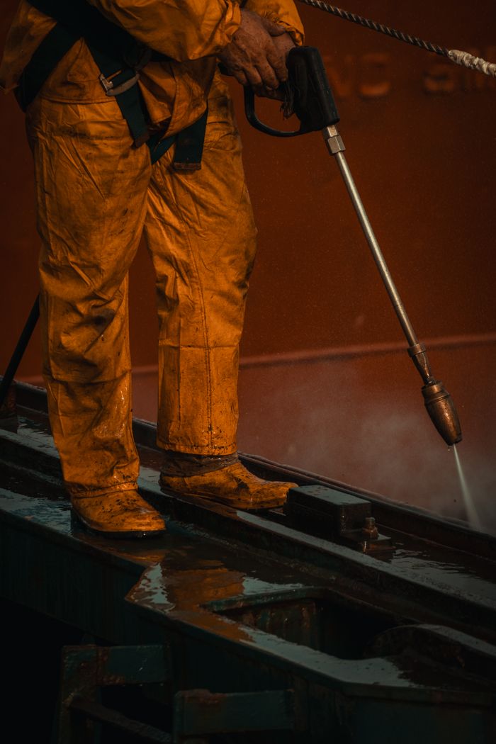 home-services-01 A worker in yellow safety gear uses a pressure washer on industrial equipment.